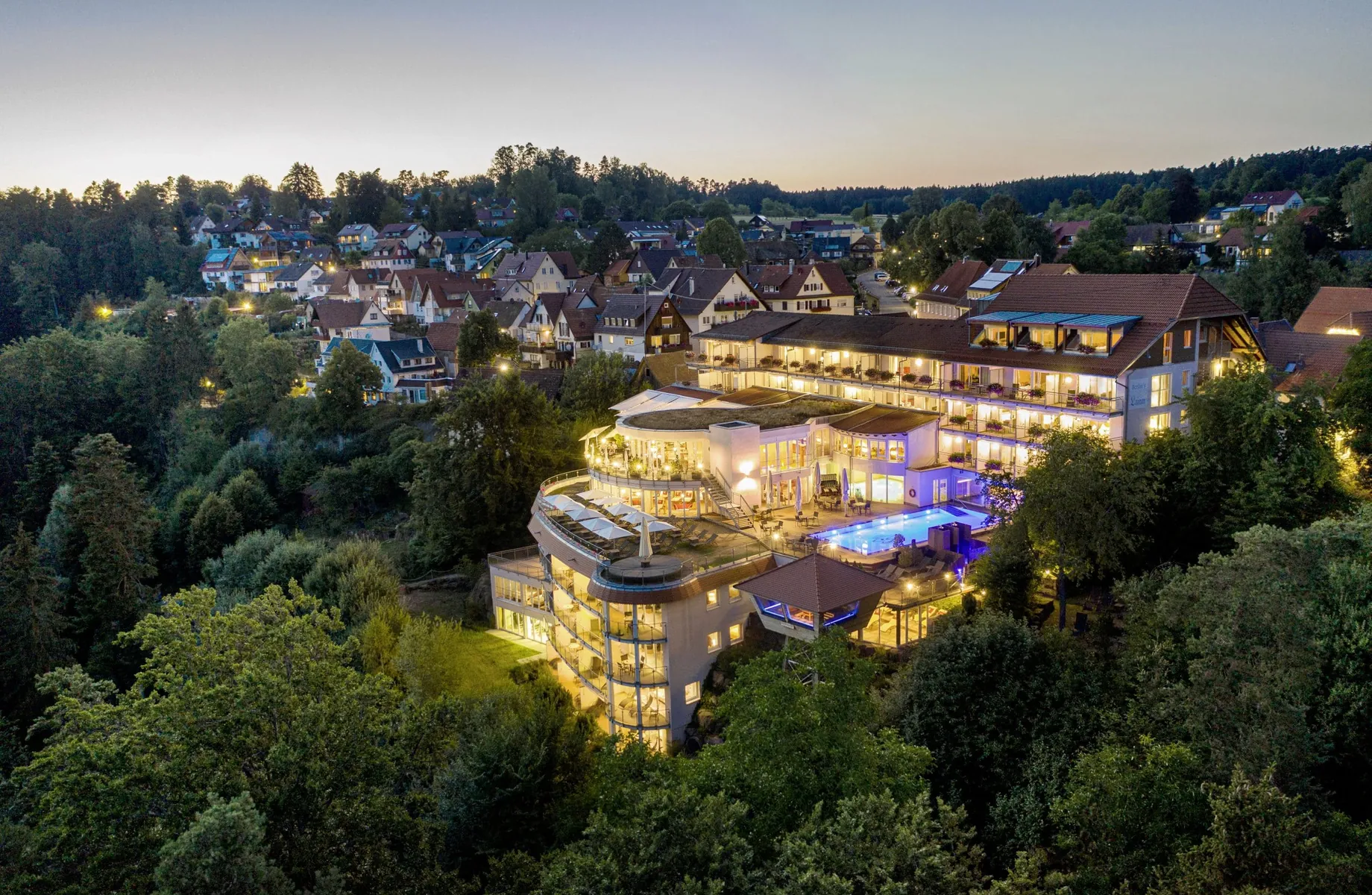 Blick aus der Luft auf das beleuchtete Wellnesshotel Kronelamm in der Dämmerung umgeben von der Natur des Schwarzwalds