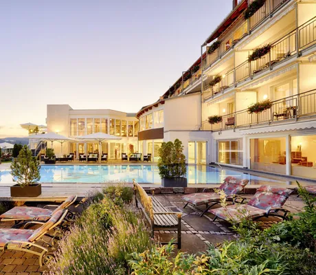 Außenansicht des Hotel Kronelamm mit Pool im Vordergrund, Liegen und weißen Sonnenschirmen