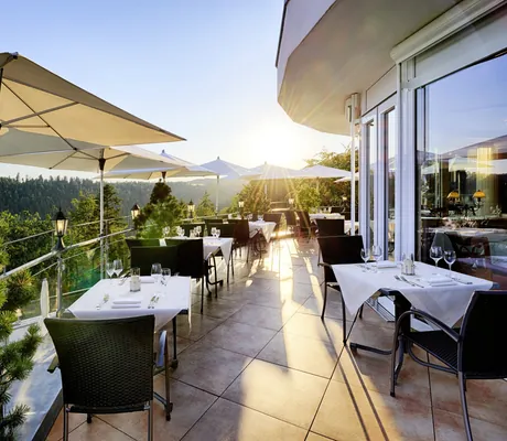 Blick auf die Terrasse des Hotel Kronelamm mit gedeckten Tischen, schwarzen Stühlen und weißen Sonnenschirmen bei strahlendem Sonnenschein