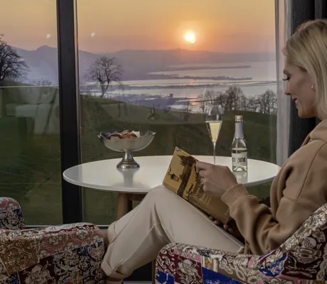 blonde Frau sitzt am Tisch im MentalSpa Resort Fritsch am Berg und liest ein Buch mit Aussicht auf den Bodensee