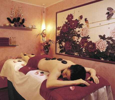 dunkelhaarige Frau liegt auf Massageliege mit Rosenblättern und heißen Steinen auf dem Rücken in Rüters Parkhotel