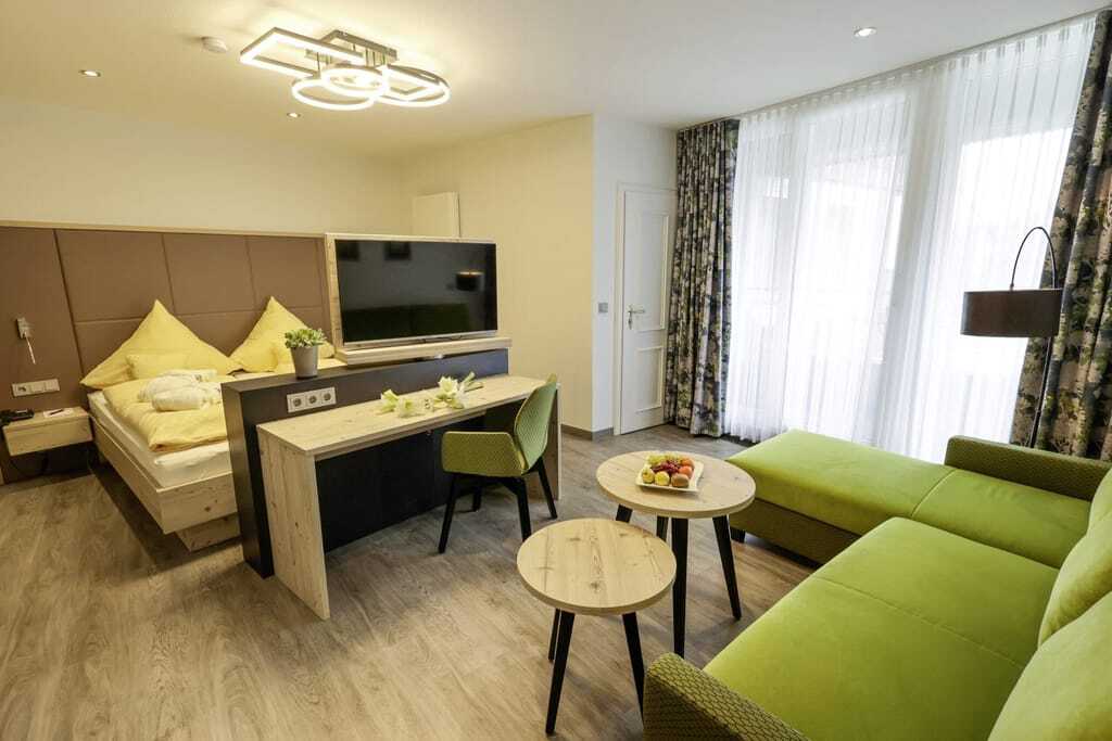 Zimmer in Rüters Parkhotel mit grünem Sofa und zwei runden Holztischen in Rüters Parkhotel
