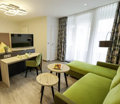Zimmer in Rüters Parkhotel mit grünem Sofa und zwei runden Holztischen in Rüters Parkhotel