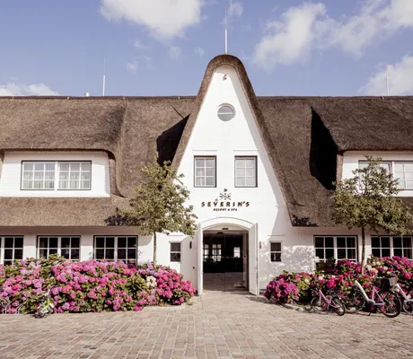 Eingang des Severin*s Resort & Spa mit reetgedecktem Dach und riesigen Hortensienbüschen