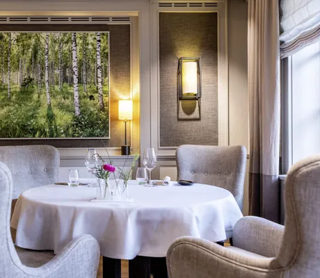 runder Tisch im Restaurant Tipken's in Severin*s Resort & Spa mit grauen Ohrensesseln und Bild vom Birkenwald