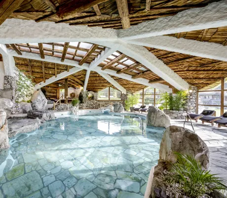 geschwungener Indoorpool im Bio- & Wellnessresort Stanglwirt mit Holzbalken an der Decke und großen Felsen am Rand