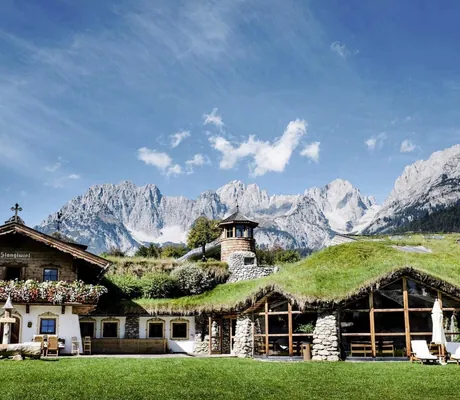 Wiese vor dem Eingang des Bio- & Wellnessresort Stanglwirt mit begrüntem Dach und Blick auf den Wilden Kaiser