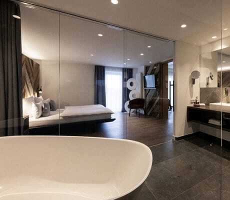 verglastes Badezimmer der Suite Sisi im Wellnesshotel Wittelsbach mit Badewanne, großem Waschbecken, Fließen in Marmoroptik und direkter Blick ins Schlafzimmer