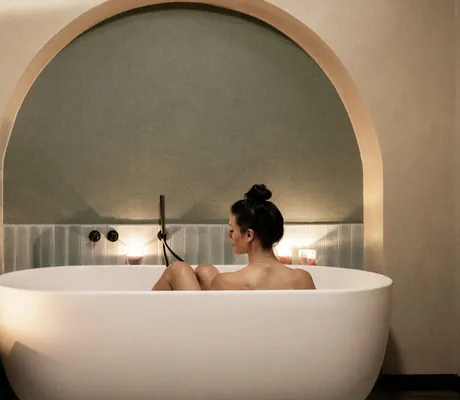dunkelhaarige Frau sitzt in einer weißen Badewanne im Wellnesshotel Wittelsbach umgeben von Kerzen