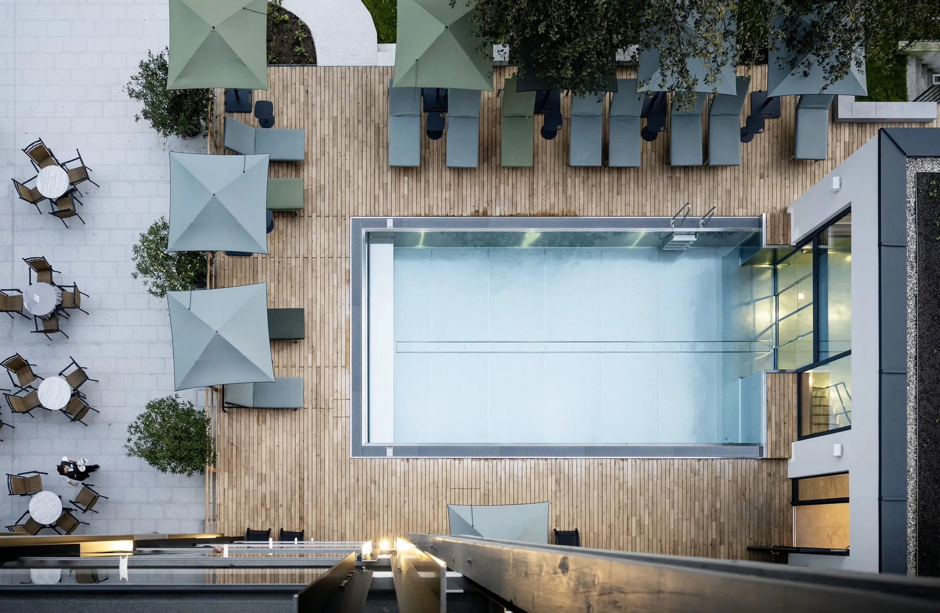 Luftaufnahme von oben des Outdoorpools mit grauen und grünen Sonnenliegen und -schirmen im Wellnesshotel Wittelsbach