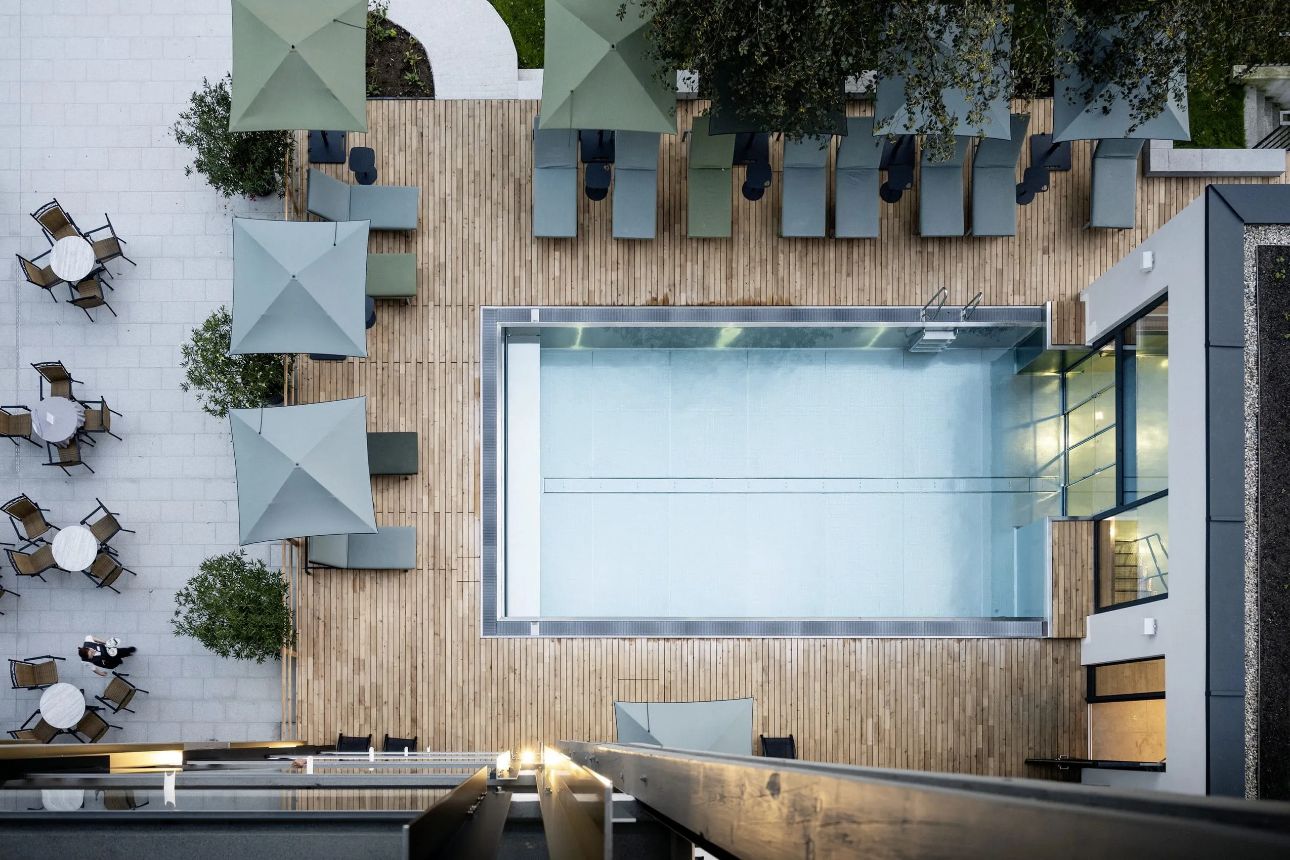 Luftaufnahme von oben des Outdoorpools mit grauen und grünen Sonnenliegen und -schirmen im Wellnesshotel Wittelsbach