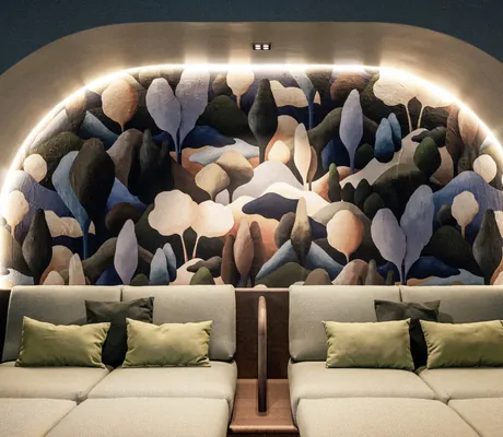 Ein gemütlicher Ruheraum im Wellnesshotel Wittelsbach mit abstrakter Waldmalerei, sanfter Beleuchtung und zwei beigen Sofas mit grünen Kissen