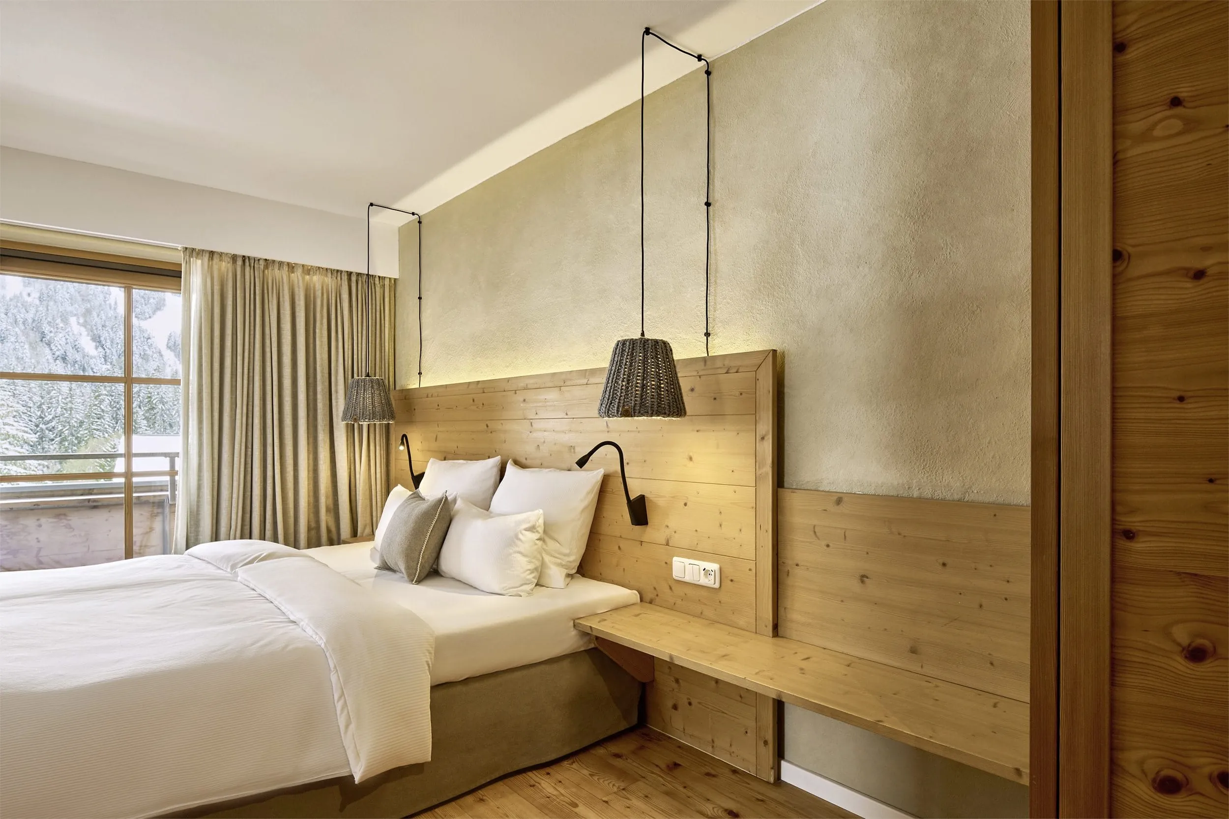 Zimmer in ruhigen Erdt&ouml;nen, die sich vom Bett, &uuml;ber die Wandfarbe bis hin zu den Vorh&auml;ngen durchzieht. Dekorative H&auml;ngelampen links und rechts neben dem Bett.