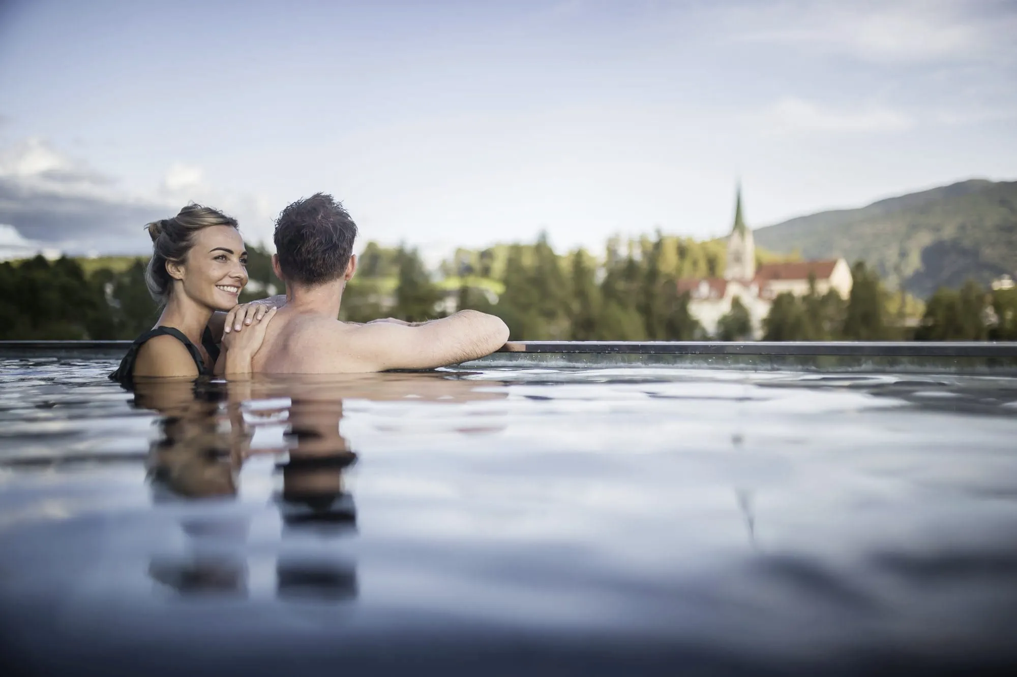 Paar am Rand des Infinitypools des Terentnerhof mit Blick auf den Kirchturm von Terenten