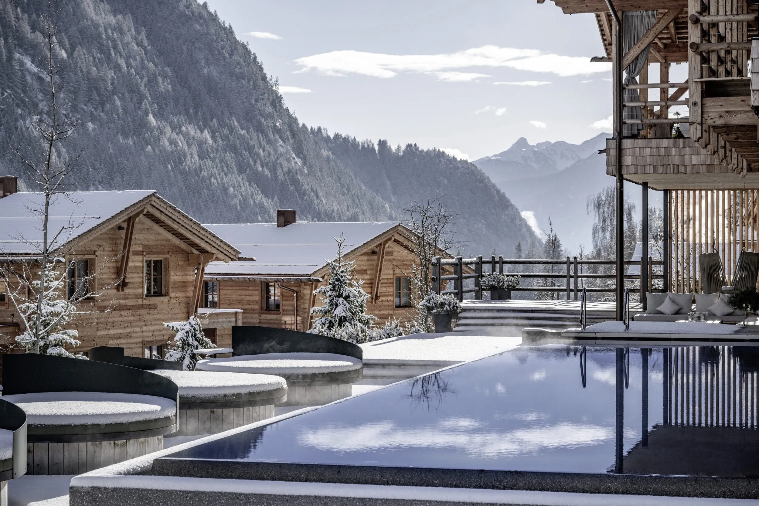 Blick auf den Outdoorpool und die mit Schnee bedeckten Dächer der Südtirol Chalets Valsegg