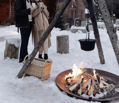 Paar steht an einer Außenfeuerstelle der Südtirol Chalets Valsegg mit Tassen in der Hand im Winter