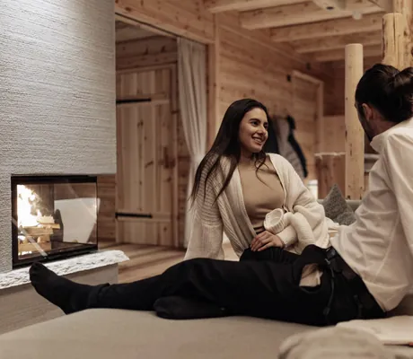 Paar sitzt auf einem gemütlichen Sofa am Kaminfeuer in den Südtirol Chalets Valsegg