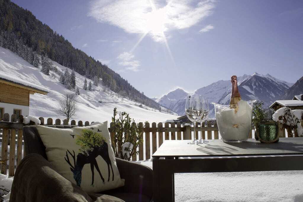 Terrasse der Hochalmbahnen Chalets im Winter mit gekühltem Sekt auf dem Tisch und Blick auf Schneelandschaft und Berge bei Sonnenschein
