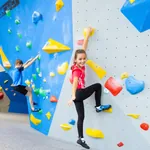 Junges Mädchen und Junge in Sportklamotten an einer Kletterwand. Das Mädchen lächelt in die Kamera, der Junge ist hochkonzentriert am klettern.