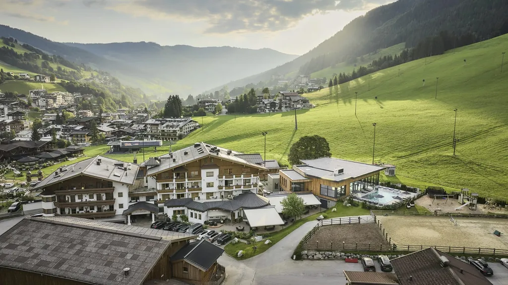 Blick auf die Hotelanlage des Bauernhof Hotel Oberschwarzach mit Outdoorpool und Reitplatz umgeben von Berglandschaft