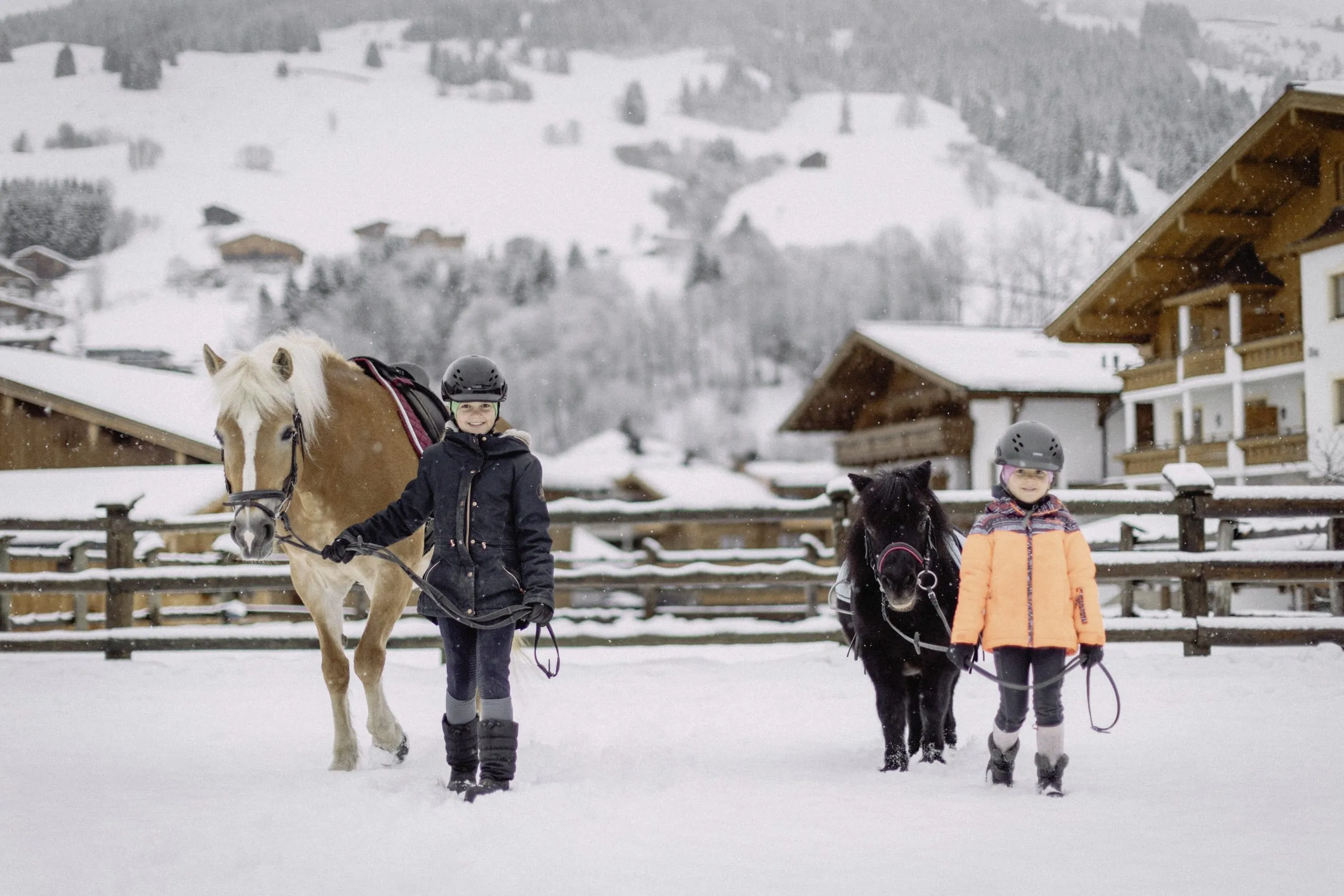 M&auml;dchen neben Pony und M&auml;dchen neben Pferd halten Strick und stehen auf der verschneiten Reitanlage des Bauernhof Hotel Oberschwarzach