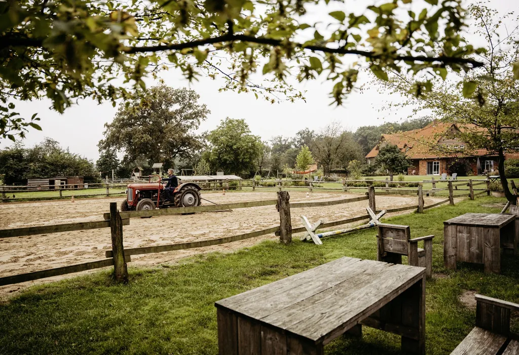 Mann auf rotem Traktor f&auml;hrt &uuml;ber den Reitplatz des Familotel Landhaus Averbeck