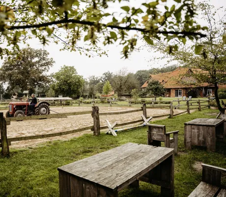 Mann auf rotem Traktor fährt über den Reitplatz des Familotel Landhaus Averbeck