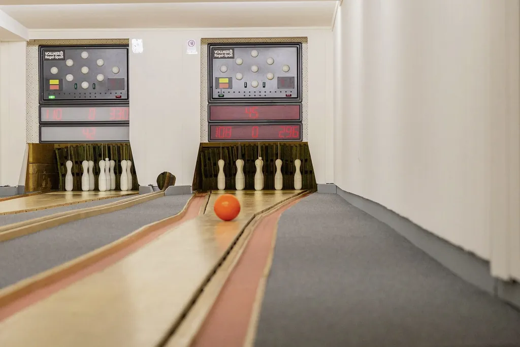 orangefarbene Bowlingkugel rollt auf wei&szlig;e Pins der Kegelbahn im Hotel Das Ebertor zu