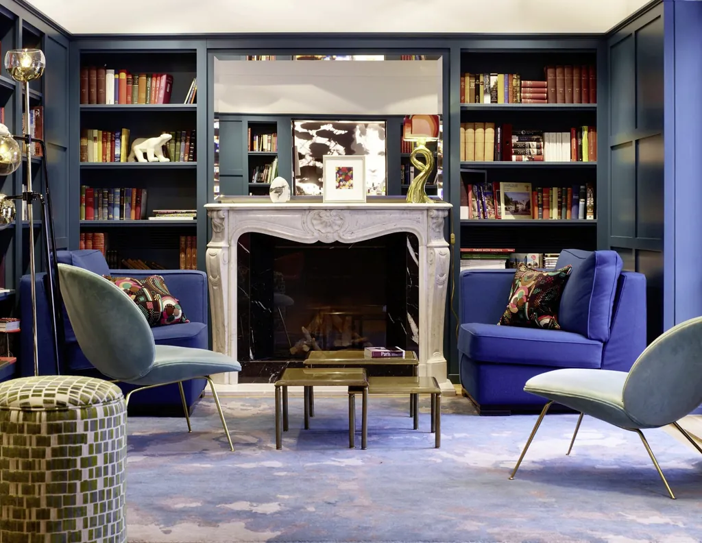 Bibliothek des LA MAISON mit blauen Sesseln und Kamin zwischen B&uuml;cherregalen