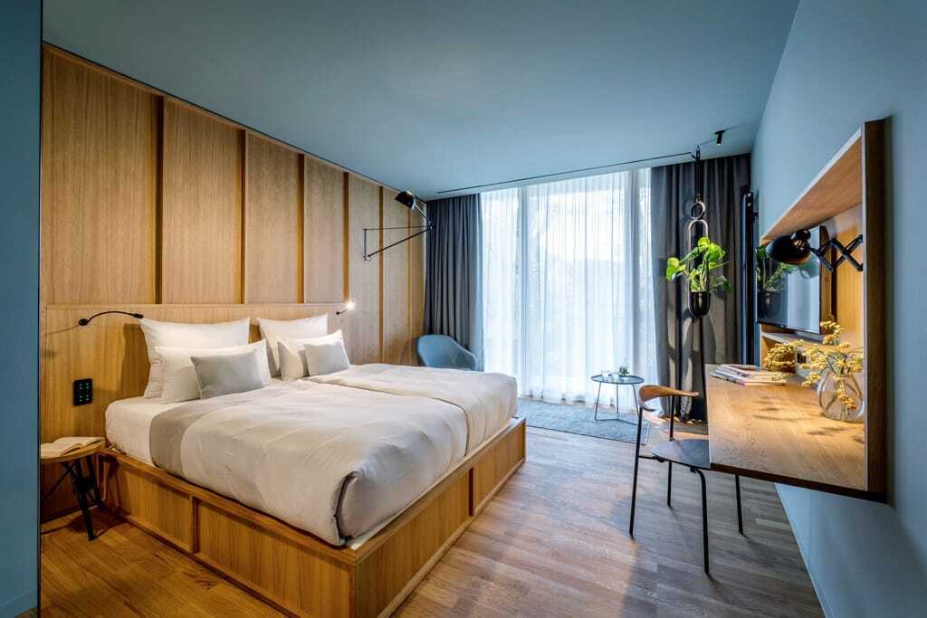 Doppelzimmer im LA MAISON mit Doppelbett aus Holz, Holzwand dahinter und blauer Wandfarbe