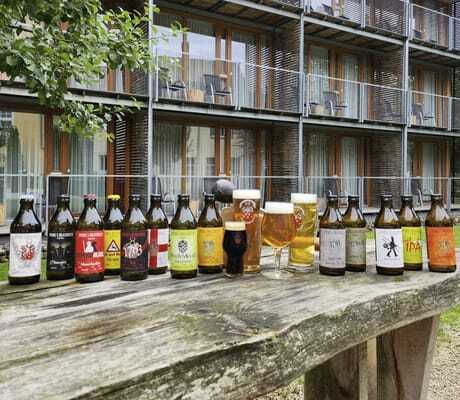 mehrere verschiedene Bierflaschen des Hotel Speidel’s BrauManufaktur stehen auf einem Holztisch vor dem Hotel