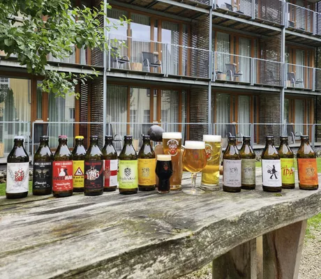 mehrere verschiedene Bierflaschen des Hotel Speidel’s BrauManufaktur stehen auf einem Holztisch vor dem Hotel