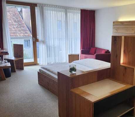 Blick in ein schlichtes Doppelzimmer des Hotel Speidel’s BrauManufaktur mit Holzeinrichtung, Doppelbett und rotem Sofa im Hintergrund