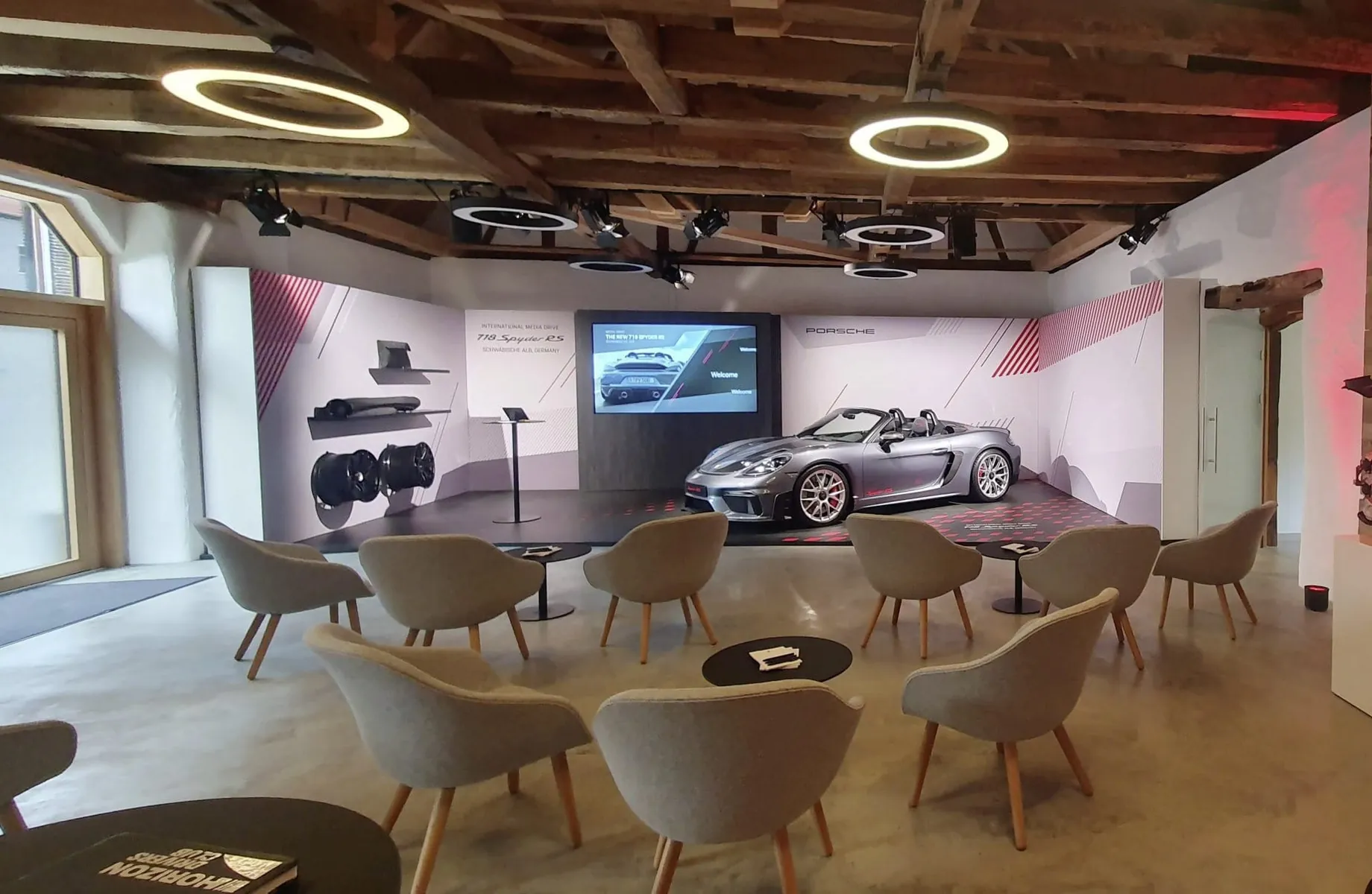 Tagungsraum des Hotel Speidel’s BrauManufaktur mit grauen Polsterstühlen, runden Ring-Deckenlampen und einem silbernen Porsche im Hintergrund