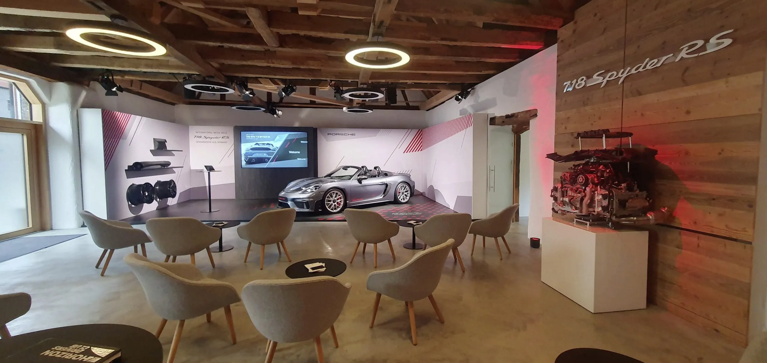 Tagungsraum des Hotel Speidel&rsquo;s BrauManufaktur mit grauen Polsterst&uuml;hlen, runden Ring-Deckenlampen und einem silbernen Porsche im Hintergrund