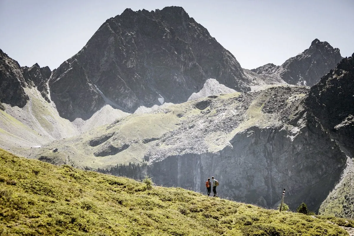 zwei Personen stehen auf Wiese vor monumentalem Felsmassiv im Tiroler Oberland