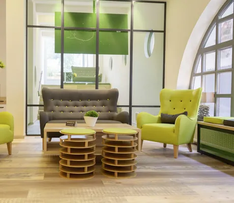 grüne Ohrensessel und graues Sofa in der Lobby des Hotel Das Ebertor vor Gitterwand