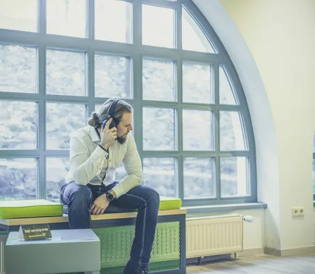 Mann mit Zopf sitzt mit Kopfhörern am halbrunden Fenster auf grünem Polster