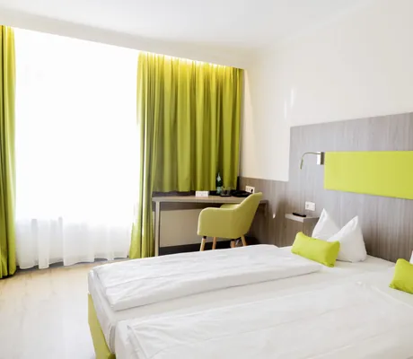 Komfortzimmer im Hotel Das Ebertor mit grünem Stoff-Bettkopf und lindgrünem Sessel