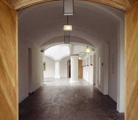 Gewölbter Gang im Schloss Hohenkammer mit Holzportal, Säulen und moderner Beleuchtung