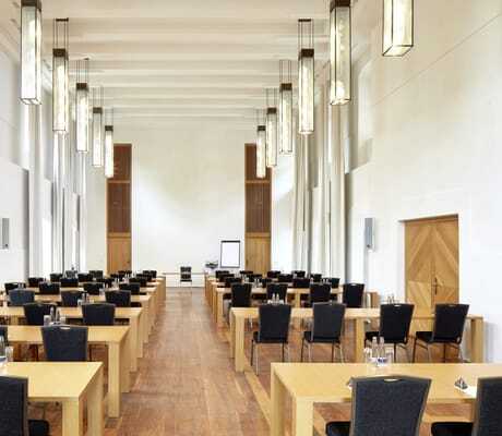 Tagungsraum des Schloss Hohenkammer, Bestuhlung in mehreren Reihen mit schwarzen Stühlen, Holztischen und hoher Decke