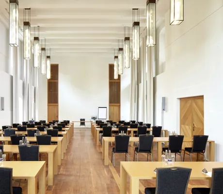 Tagungsraum des Schloss Hohenkammer, Bestuhlung in mehreren Reihen mit schwarzen Stühlen, Holztischen und hoher Decke