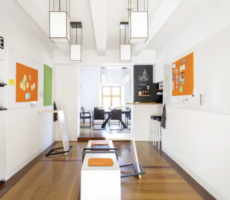 Moderner Tagungsraum im Schloss Hohenkammer mit weißen Wänden, orangefarbenen Magnettafeln und Tisch mit schwarzen Stühlen im Hintergrund