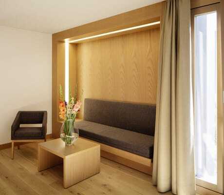 Blick in ein Zimmer des Schloss Hohenkammer mit gepolsterter Sitzbank, Polsterstuhl, kleinem Holz-Beistelltisch mit Blumenvase und Doppelbett im Hintergrund