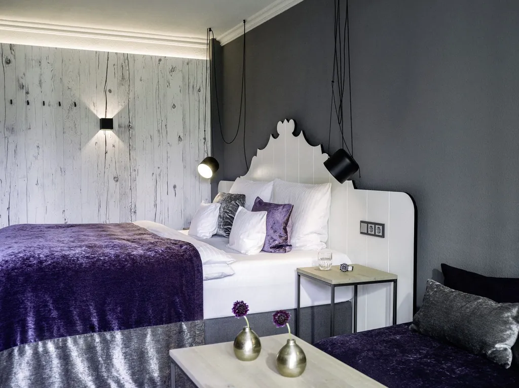Zimmer im Das König Ludwig Inspiration Spa mit weißem verschnörkeltem Bettkopf und lila Tagesdecke