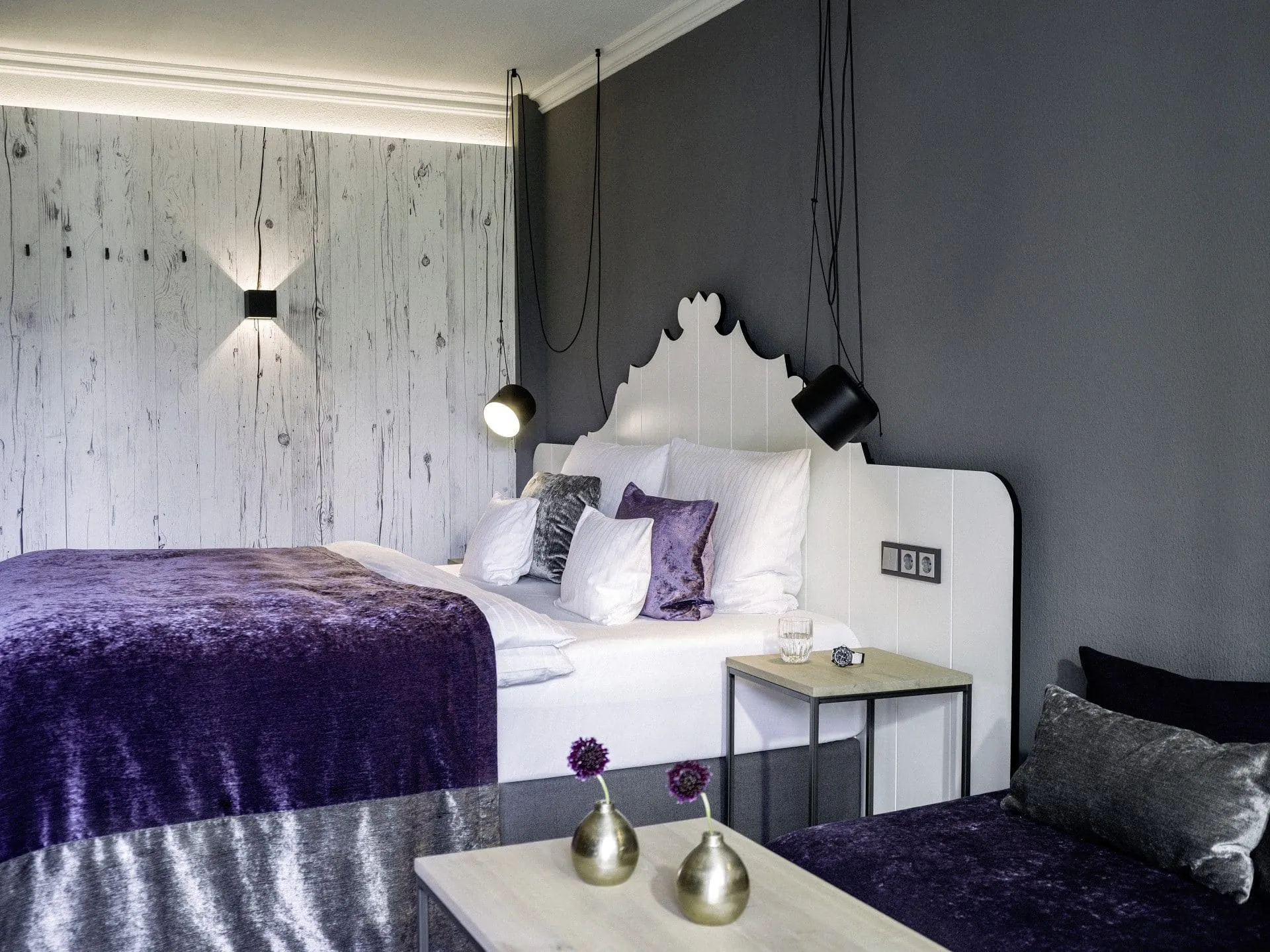 Zimmer im Das K&ouml;nig Ludwig Inspiration Spa mit wei&szlig;em verschn&ouml;rkeltem Bettkopf und lila Tagesdecke