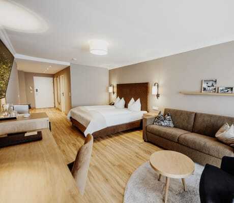 großes Doppelzimmer im Hotel Post Seefeld mit Holzboden und braunem Sofa