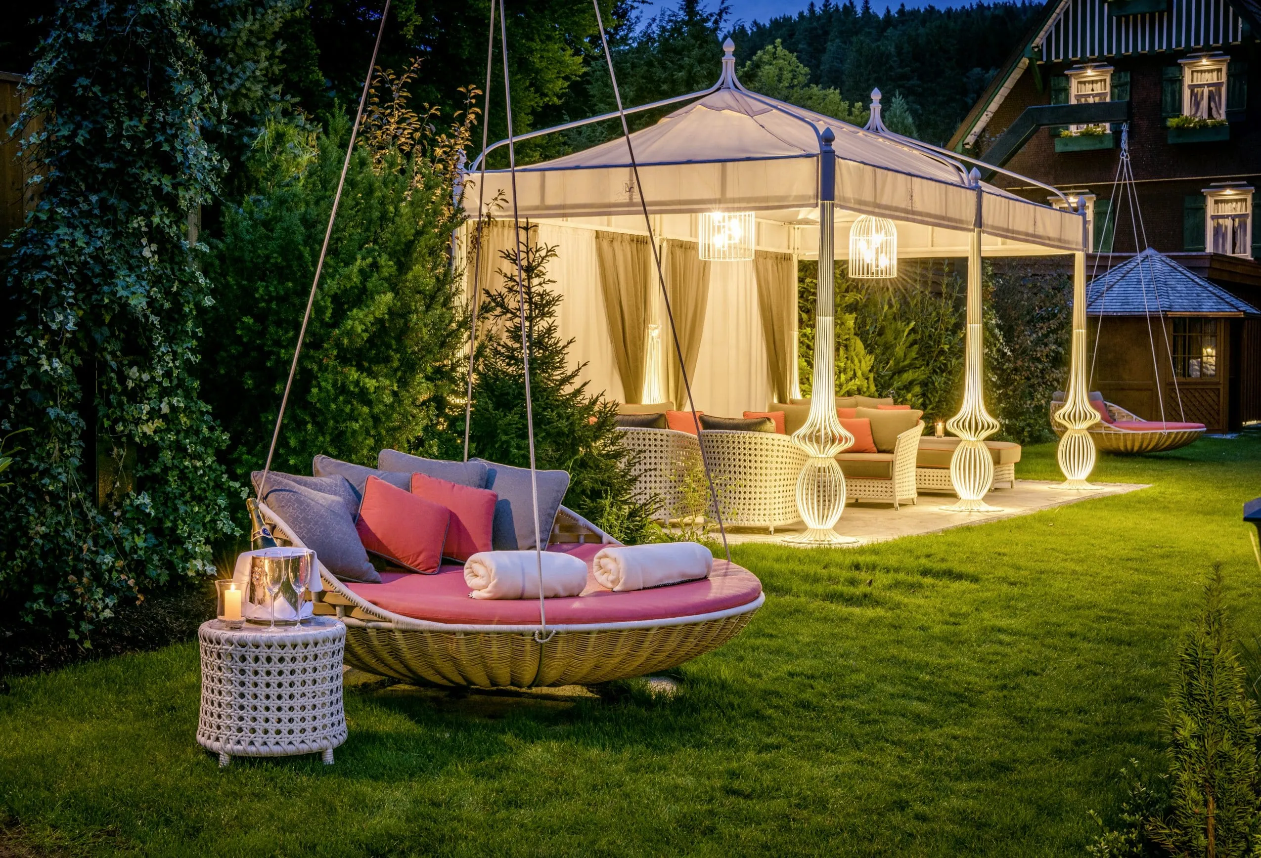 Liegewiese des Hotel Bareiss mit gem&uuml;tlichen H&auml;ngeschaukeln und illuminiertem Pavillon mit Loungebereich