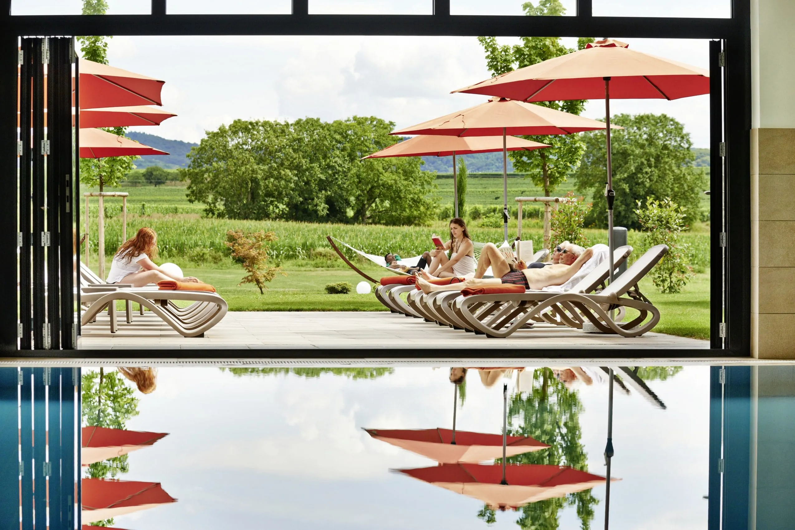 Blick vom Innenpool des Kreuz-Post Wellnesshotels auf Relaxliegen im Outdoor-Bereich