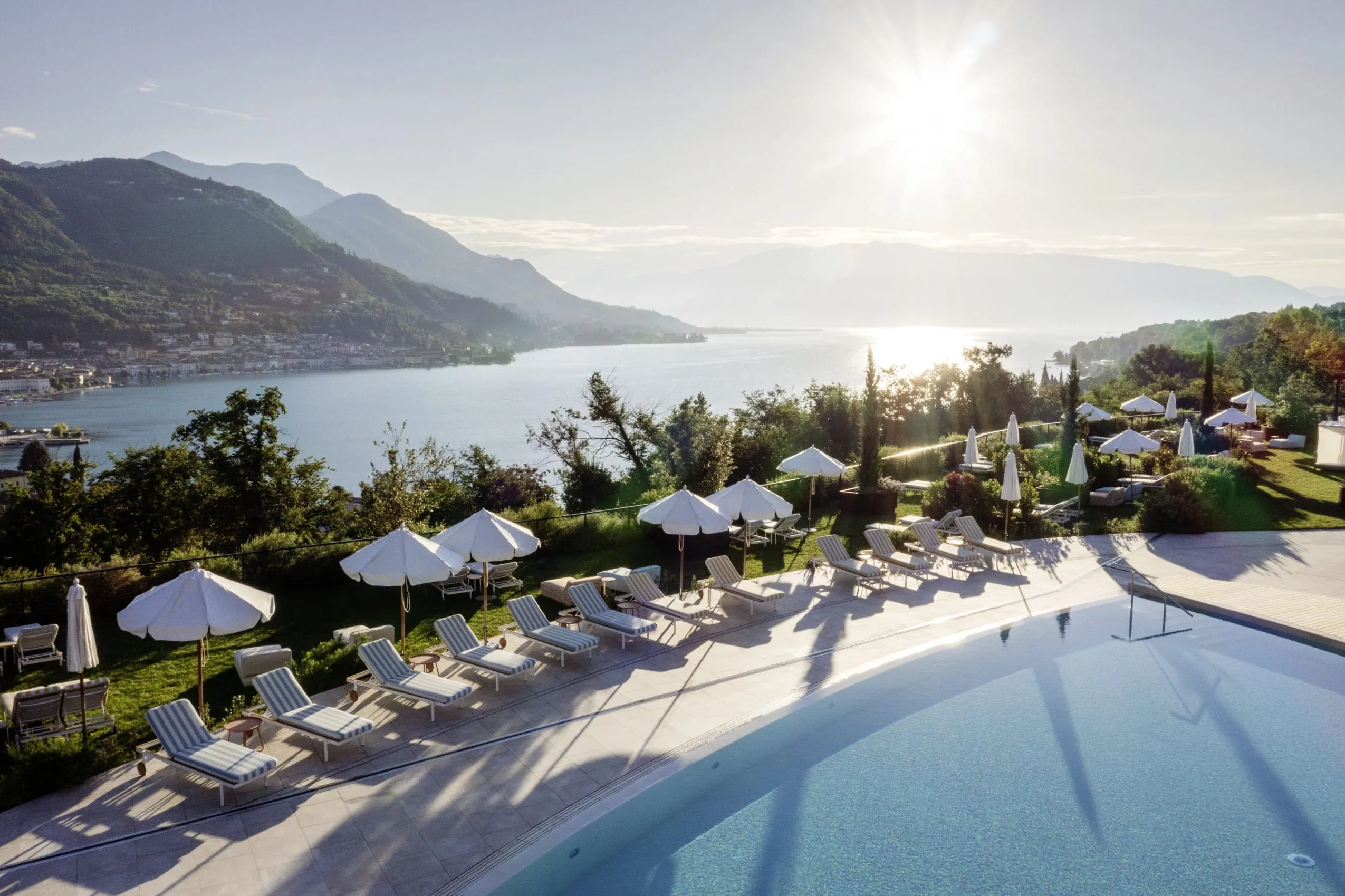 Blick &uuml;ber den Outdoorpool mit seinen wei&szlig;en Sonnenschirmen des A-ROSA Gardasee auf den See